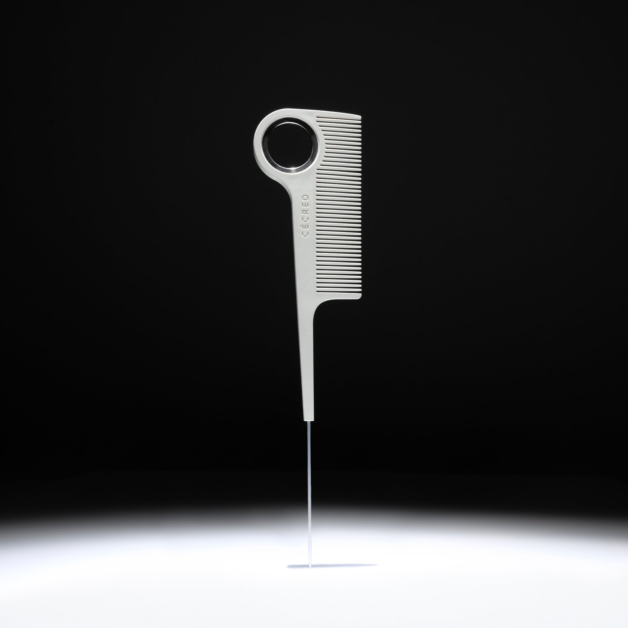 Cécred rat tail comb with stainless steel tail displayed upright against a black background.