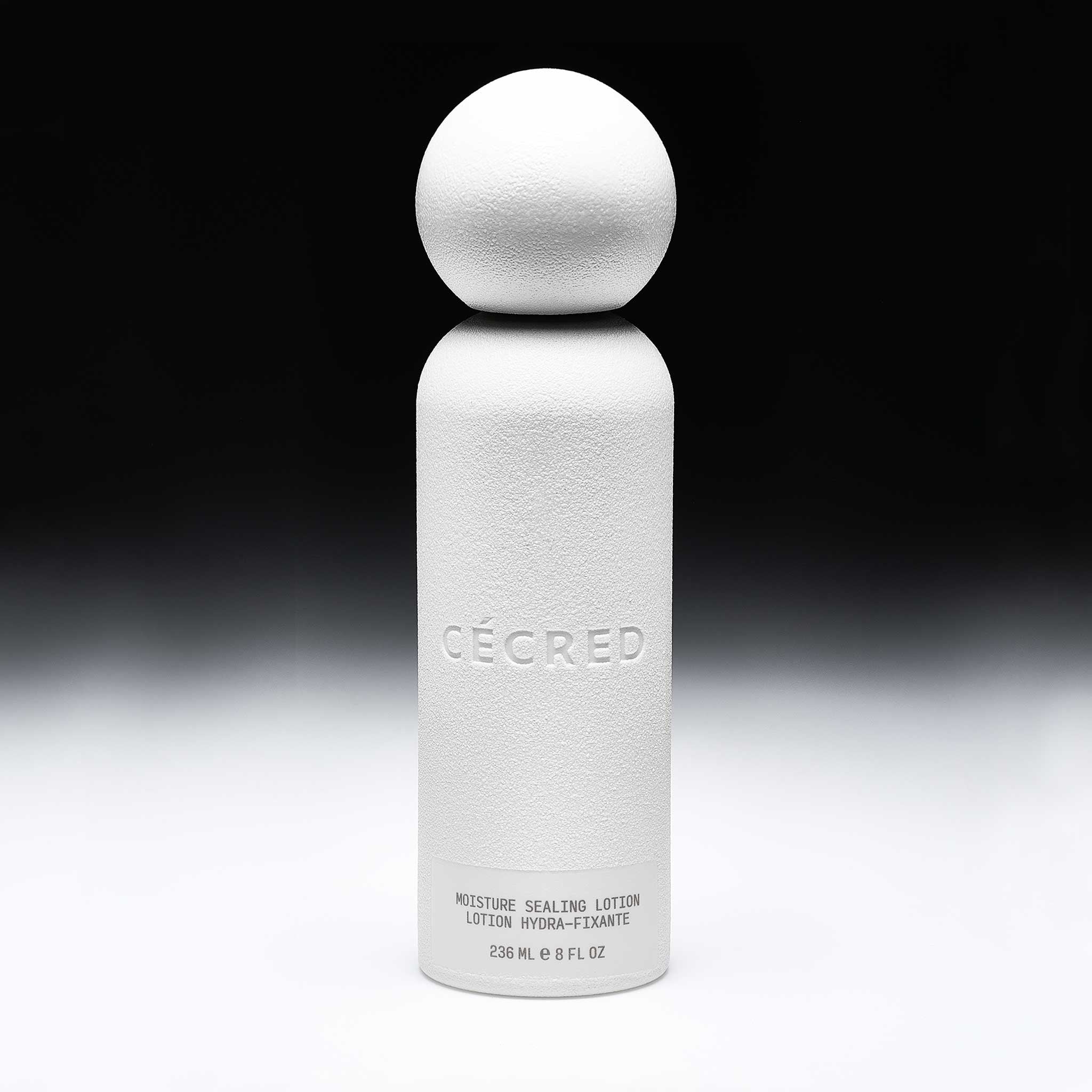 Cécred Moisture Sealing Lotion full bottle shown against a black and white gradient background, spotlighting its unique round cap and matte white texture