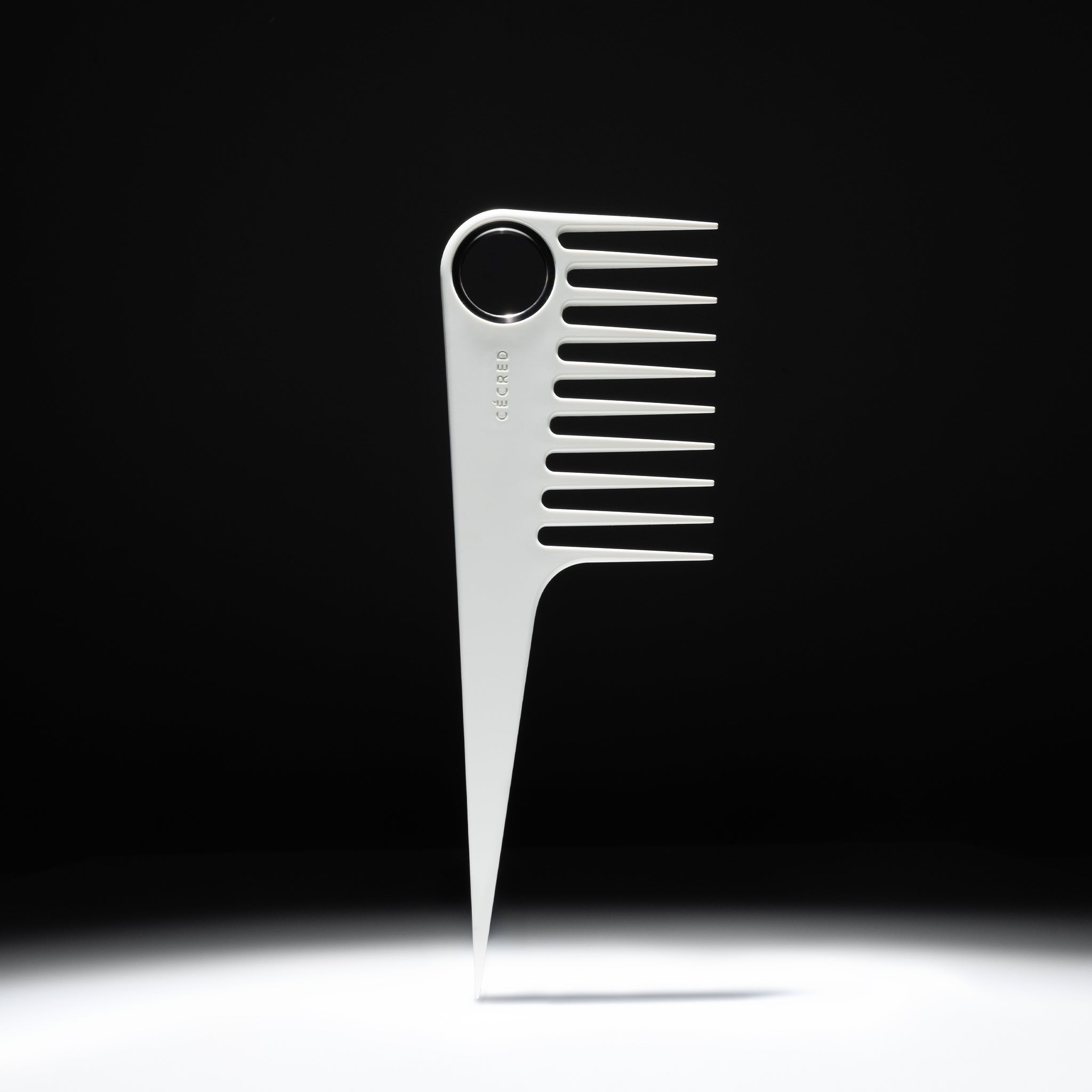 Cécred wide-tooth comb with circular handle and pointed tail displayed upright against a gradient black background, showcasing its sleek matte white design